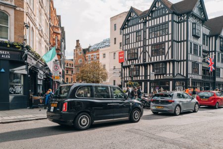 Foto de Londres, Reino Unido - 13 de abril de 2023: Moderno taxi negro eléctrico en una calle en Soho, Londres. Los taxis negros son una parte importante del sistema de transporte de la capital. - Imagen libre de derechos