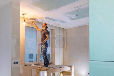 Téléchargez les photos : Travailleur faire des réparations dans un nouvel appartement. Homme plâtre murs et plafonds. Photo de haute qualité - en image libre de droit