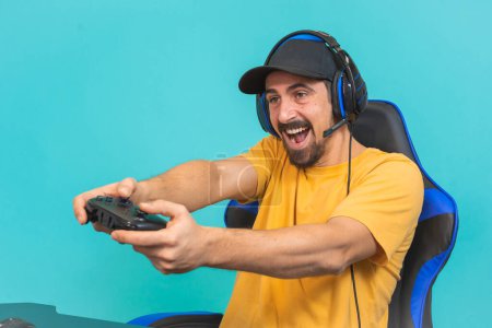 Excited young gamer man playing games holding joystick isolated on blue wall background studio portrait. Millenial guy play station . High quality photo