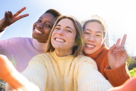 Téléchargez les photos : Group of three multiethnic smiling friends taking a selfie outdoors during sunset. Students college campus life. High quality 4k footage - en image libre de droit