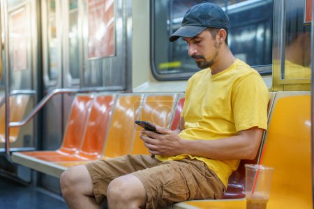 Téléchargez les photos : Un jeune homme assis dans le métro de New York envoie des textos et utilise un téléphone pour lire sa correspondance. Touriste adulte à Manhattan, États-Unis. Photo de haute qualité - en image libre de droit