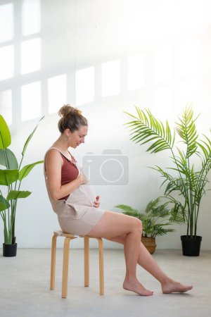 Téléchargez les photos : Femme enceinte touchant le ventre à la maison. Préparation à l'accouchement, conseils nutritionnels pour une grossesse en bonne santé. Photo verticale avec espace de copie pour le texte. Photo de haute qualité - en image libre de droit