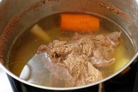 Leckere Rindfleischbrühe mit Fleisch und Gemüse im Kochtopf langsam kochend zubereiten