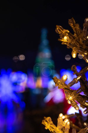Photo for A photograph of a tall Christmas tree decoration made of lights out of focus in the background with other holiday lights in focus in the foreground. - Royalty Free Image