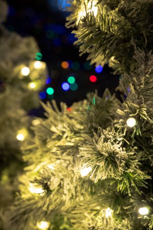 Foto de Fotografía de cerca de las ramas de un árbol de Navidad artificial con luces en primer plano con colorida luz de vacaciones bokeh de decoraciones en el fondo haciendo un telón de fondo festivo. - Imagen libre de derechos