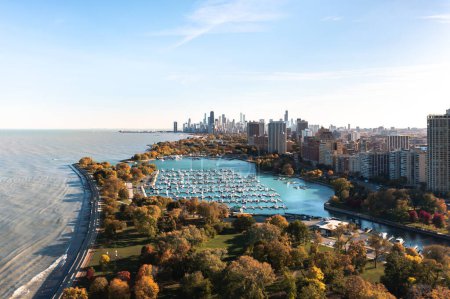 Beautiful aerial photograph of the Chicago skyline overlooking Belmont Harbor and the lakefront below on a sunny autumn day with fall colored foliage below.