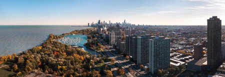 Téléchargez les photos : Beautiful cityscape aerial panorama of the Lakeview neighborhood lakefront with autumn foliage surrounding Belmont Harbor and the Chicago skyline in the distance on a sunny day. - en image libre de droit