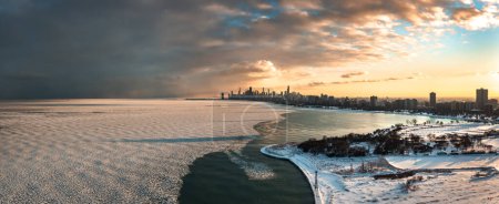 Téléchargez les photos : Beautiful aerial panorama view of the downtown Chicago skyline from above Lake Michigan near Montrose Beach with frozen ice chunks floating on the waves below at sunset. - en image libre de droit