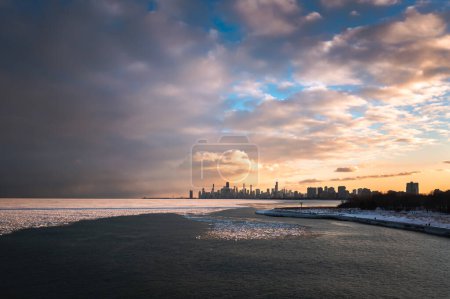 Photo for Aerial view of downtown Chicago Skyline from above the icy cold water of Lake Michigan in winter as the sunset colors the blue sky and clouds with orange and yellow hues. - Royalty Free Image