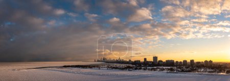 Téléchargez les photos : Wide angle aerial panorama of the north side of Chicago from above the frozen water of Lake Michigan overlooking the Uptown and Lakeview neighborhoods towards downtown at sunset with cloudy sky above. - en image libre de droit