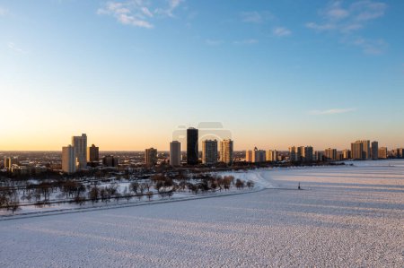 Photo for Beautiful aerial photograph of the residential highrise buildings in the Edgewater neighborhood as the buildings and bare trees cast shadows over the frozen and snow covered Lake below at sunset. - Royalty Free Image