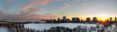 Téléchargez les photos : Beautiful sunset aerial panorama of cricket hill with the sun setting behind residential highrise buildings in the Uptown neighborhood with the downtown skyline in the distance and pink clouds above. - en image libre de droit