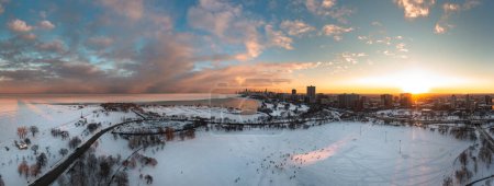 Téléchargez les photos : Beautiful aerial sunset panorama of the north side of Chicago at sunset with people sledding down a snow covered hill below and sun setting behind the Uptown neighborhood skyline. - en image libre de droit