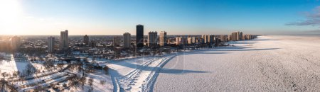 Téléchargez les photos : Beautiful aerial panorama of the residential highrise buildings casting shadows onto a frozen Lake Michigan at sunset with snow covering both the water and shoreline below. - en image libre de droit