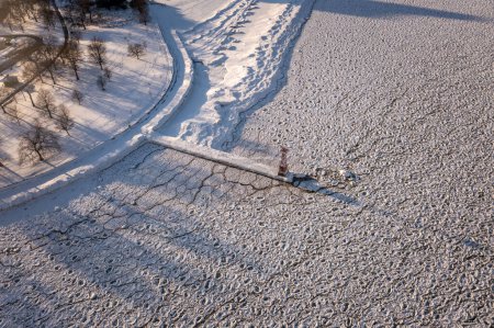 Téléchargez les photos : Beautiful aerial winter scene of a pier and tower extending out into an ice covered Lake Michigan near Foster beach in Chicago with bare trees and snow covering the ground along the shore at sunset. - en image libre de droit
