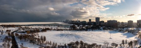 Foto de Beautiful winter aerial panorama photograph of people sledding in the snow on Cricket hill near Montrose Harbor with clouds over the downtown Chicago skyline in the distance at sunset. - Imagen libre de derechos