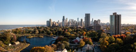 Photo for Chicago, IL - October 19th, 2022: Bright red and yellow fall tree foliage surrounds the barn and South Pond in the Lincoln Park neighborhood as nearby high-rise buildings cast shadows over the area. - Royalty Free Image