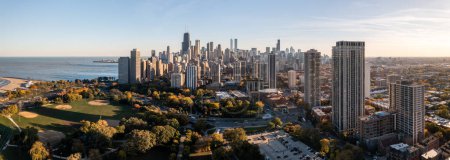 Foto de Chicago, IL - October 19th, 2022: The ball fields sit empty and quiet amongst a forest of autumn colored trees and high rise buildings casting shade over Lincoln Park on a blue sky afternoon. - Imagen libre de derechos