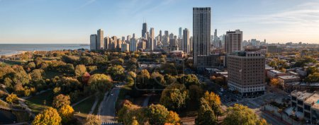 Photo for Chicago, IL - October 19th, 2022: Shades of yellow and red set in on the tree covered landscape as the sun shines between high-rise buildings as it sets over the Lincoln Park neighborhood. - Royalty Free Image