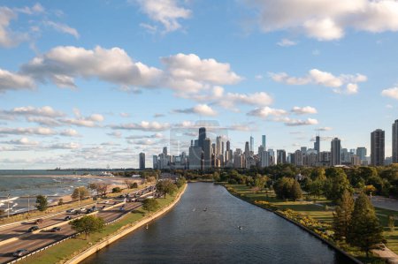 Foto de Aerial view of downtown Chicago skyline as a few people use the South Lagoon canal for boating and rowing below on a sunny day with blue sky and fluffy white cumulus clouds above. - Imagen libre de derechos