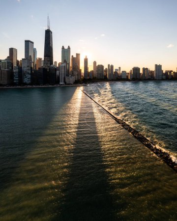 Téléchargez les photos : Beautiful downtown Chicago skyline aerial drone photograph above Lake Michigan during the  autumn equinox as the sun casts a glistening yellow glow and long building shadows over the water below. - en image libre de droit