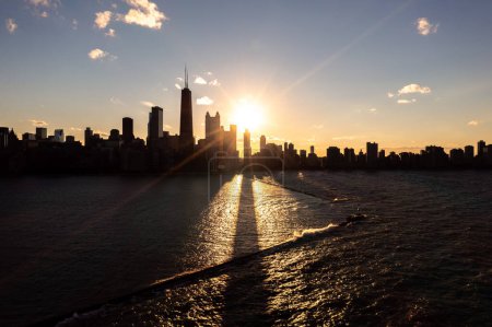 Foto de Beautiful downtown Chicago skyline aerial over the Lake Michigan breakwater during the  autumn equinox sunset casting a glistening yellow glow and long shadows from buildings over the water below. - Imagen libre de derechos