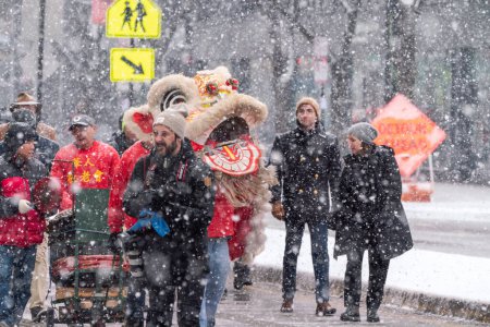 Téléchargez les photos : Chicago, IL - January 28th, 2023: A photographer pulls out a rag to wipe his gear during the annual Argyle Lunar New Year parade as a band and lion dancer makes their way down Broadway in the snow. - en image libre de droit