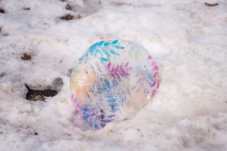Téléchargez les photos : Close up garbage or litter photograph of a colorful lost stray leaf patterned clear balloon partially deflated and laying in the melting snow. - en image libre de droit