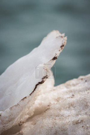 Téléchargez les photos : Close up of a delicate thin white snowy ridge laced with dirt and sand formed from melting snow and ice along the lakefront with blue water in background on a sunny day making a great winter backdrop. - en image libre de droit