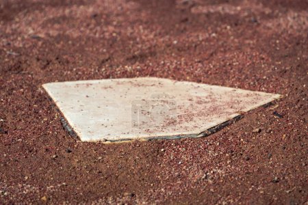 Téléchargez les photos : Gros plan d'une base d'assiette de baseball blanche dans un champ de saleté et de boue marron ou rouge mouillé sur un terrain de baseball vide par une journée ensoleillée. - en image libre de droit