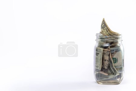 Photo for Isolated overflowing glass mason jar stuffed full of cash or USD paper currency as a financial savings or investment concept positioned to the right side with white background and copy space. - Royalty Free Image