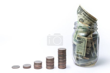 Exponential savings or investment growth concept with increasing piles of stacked quarters leading up to a glass jar full of cash making a great financial background isolated on white with copy space.