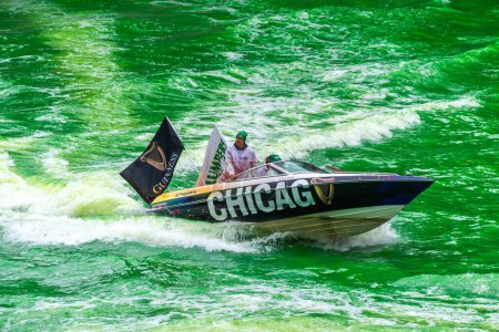 Téléchargez les photos : Chicago, IL - 11 mars 2023 : Le bateau de bière Guinness du syndicat local 130 du plombier avec des drapeaux battant pavillon dans le vent navigue dans l'eau vert vif de la rivière Chicago fraîchement teinte créant un sillage. - en image libre de droit