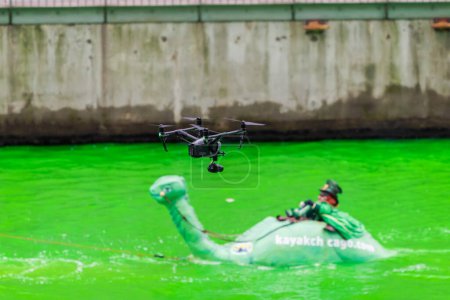 Photo for Chicago, IL - March 11th, 2023: A professional drone pilot hovers their drone over the iconic Kayak Chicago Loch Ness Monster and Leprechaun passenger during the St. Patrick's day river dyeing event. - Royalty Free Image