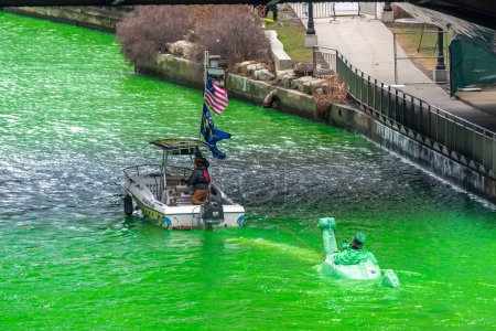 Foto de Chicago, IL - 11 de marzo de 2023: Un barco remolca un barco monstruo loch ness sosteniendo a un hombre vestido de duende durante el evento anual de teñido del río verde en el centro de la ciudad. - Imagen libre de derechos