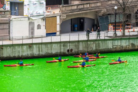 Foto de Chicago, IL - 11 de marzo de 2023: Un grupo de kayaks de color rojo bordean el río durante el evento anual de teñido del río verde para el día de San Patricio mientras el personal de seguridad se para en la cercana caminata por el río. - Imagen libre de derechos