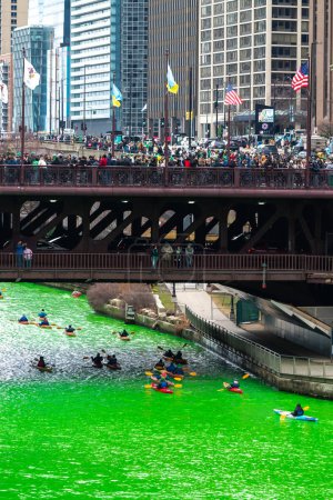 Foto de Chicago, IL - 11 de marzo de 2023: Un tour en kayak pasa por debajo del puente DuSable mientras multitudes de personas observan desde Michigan Avenue durante el evento anual de teñido del río verde del día de San Patricio. - Imagen libre de derechos