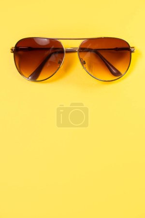 Téléchargez les photos : Gros plan de lunettes de soleil de style aviateur avec des teintes brunes centrées au sommet d'un fond jaune vif coloré faisant une toile de fond d'été fantastique avec espace de copie. - en image libre de droit