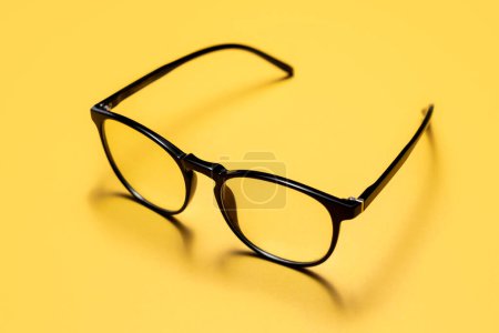 Photo for Close up photograph of a pair of light filtering reading glasses or spectacles with black modern minimalistic plastic frames on a bright yellow background. - Royalty Free Image