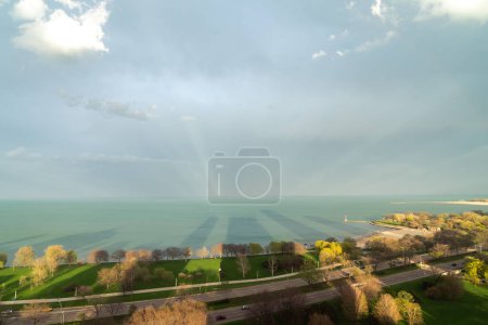 Téléchargez les photos : Beau paysage panoramique aérien du lac Michigan au coucher du soleil alors que le soleil projette de longues ombres de construction sur le parc convergeant avec des rayons lumineux projetés sur les nuages de tempête bleue au-dessus. - en image libre de droit