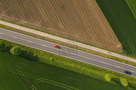 Téléchargez les photos : Vue aérienne de la route à deux voies à travers la campagne et les champs cultivés avec des voitures. Drone shot - en image libre de droit