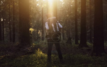 Téléchargez les photos : Randonneur debout dans la forêt et regardant le coucher du soleil sur les arbres - en image libre de droit