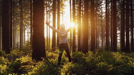 Téléchargez les photos : Jeune homme mains levées debout dans la forêt et jouit de la nature et de la lumière du soleil - en image libre de droit
