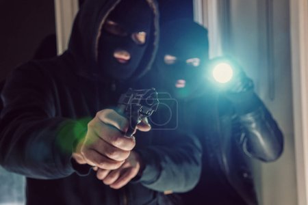 Téléchargez les photos : Cambrioleur masqué avec arme à feu entrant par effraction dans la maison d'une victime - en image libre de droit