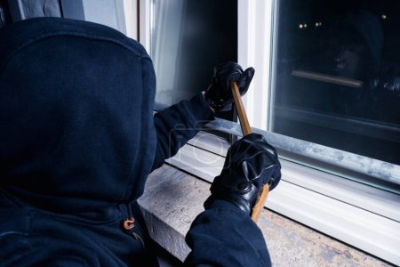 burglar opens a window with a crowbar at night