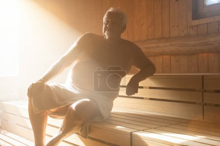Foto de Hombre en la Sauna. Vapor con luz solar, spa y concepto de bienestar, relajarse en la sauna finlandesa caliente. - Imagen libre de derechos
