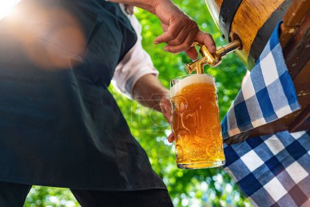 Bavarois homme dans le tablier verse une grande bière blonde dans le robinet du tonneau de bière en bois dans le jardin de la bière. Contexte pour Oktoberfest, festival folklorique ou de la bière (en allemand pour : Ozapft est!) 