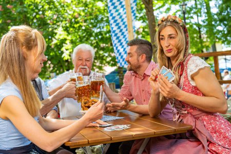 Photo for Bavarian people in traditional costume playing traditional card game of Schafkopf in a German beer garden or oktoberfest - Royalty Free Image
