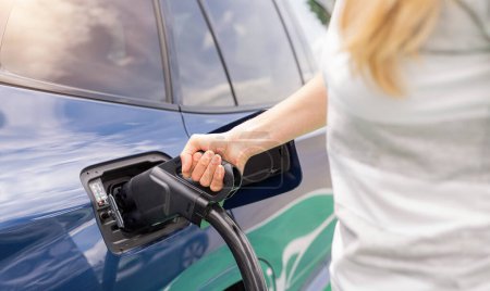 Woman inserting a DC CCS2 EV charging connector into electric car socket at charging station, Hypercharger or Supercharger.  Charge electromobility concept image.