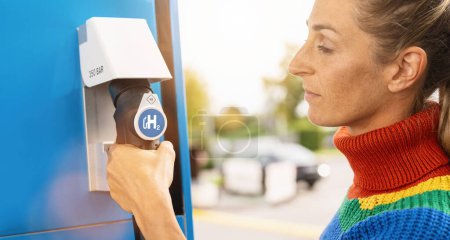 Photo for Woman holds a fuel dispenser with hydrogen logo on gas station to fill up her car. h2 combustion engine for emission free eco friendly transport concept image - Royalty Free Image